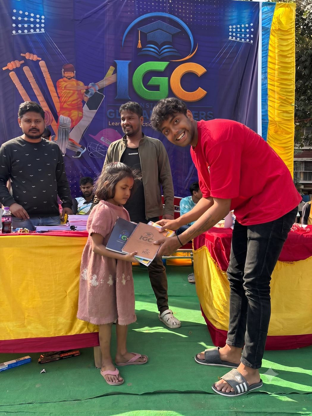 IGC volunteer handing a study material booklet and tote bag to a child and parent